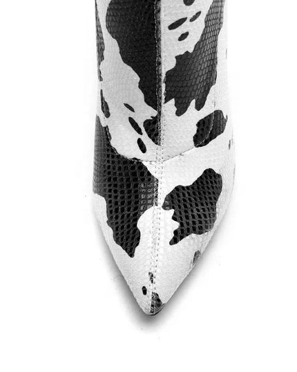 Bottines femme à talons aiguilles avec imprimé vache blanc. Fermeture éclair latérale, bout pointu. Disponibles en grandes tailles.